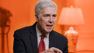 Justice Gorsuch speaks to Nick Gillespie against a bright orange background. | Reason