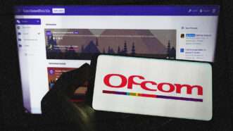A hand holds a phone with the Ofcom logo on it, in front of a computer monitor open to the Sanctioned Suicide webpage. | Illustration: Timon Schneider/Dreamstime/Sanctioned Suicide