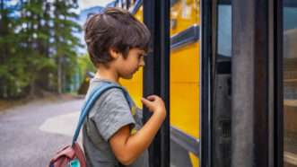 A young boy tentatively gets on a yellow school bus. | imageBROKER/Unai Huizi/Newscom