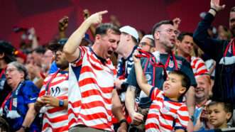 Fans of all ages and various races celebrate in the stands, wearing U.S. Soccer jerseys with wavy red stripes. | Photo: Billy Schuerman/Cal Sport Media/Newscom