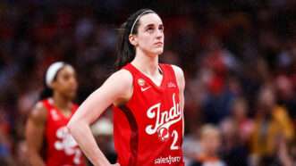 Caitlin Clark stands with her hands on her hips in a basketball arena, wearing a red Indiana Fever jersey. | Jeffrey Brown/Icon Sportswire DBF/Jeffrey Brown/Icon Sportswire/Newscom