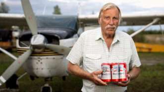 Ken Jouppi holds a six-pack of beer while standing in front of his airplane | Institute for Justice