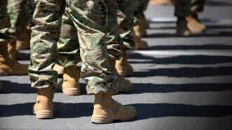 Several uniformed service members wearing camouflage pants and tan combat boots stand in formation. | Photo: Ilia Torlin/Dreamstime.