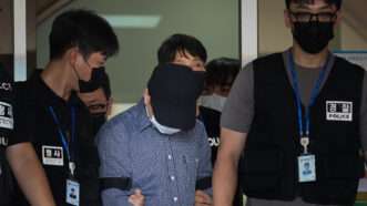 South Korean police officer only identified by the surname Bu. His head is down and he wears a dark blue baseball cap as officers lead him away in handcuffs. |  Yonhap News/YNA/Newscom