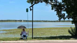 A man sitting in a lawn chair hoists a small placard to obscure a surveillance camera | Photo: Valerie Smith/Creative Loafing Tampa Bay