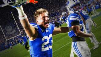 A few BYU football players celebrate on the field, one of them has ripped off his helmet. | Aaron Baker/Icon Sportswire CHE/Aaron Baker/Icon Sportswire/Newscom