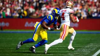 A San Francisco 49ers runs away from the camera with a football, while a Los Angeles Rams player tries to tackle him. | Photo: Chris Putnam/ZUMAPRESS/Newscom