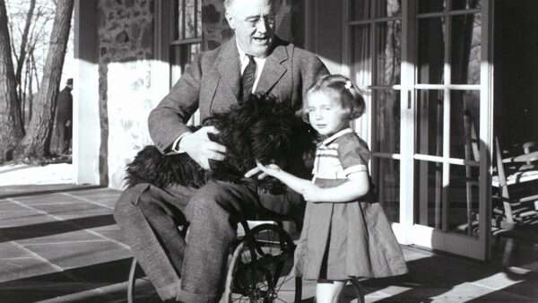 Franklin Roosevelt sitting in a wheelchair with a dog on his lap and a young girl at his side | Photo: President Franklin Roosevelt, 1941; CBW/Alamy