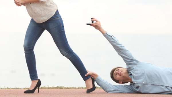 A man lying on the ground holding a woman's foot as she walks away from him. He's holding up an engagement ring. | Antonio Guillem Fernández/Newscom