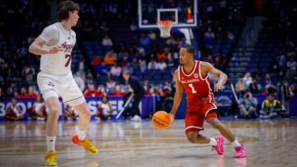 A player in an Oklahoma Sooners basketball jersey is dribbling near a player in a Texas A&M Aggies jersey—in the background is a basketball hoop and fans sitting in the stands. | Photo: Matthew Maxey/Icon Sportswire DHH/Matthew Maxey/Icon