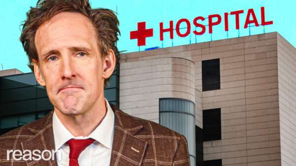 Andrew Heaton with a hospital behind him. | ReasonTV