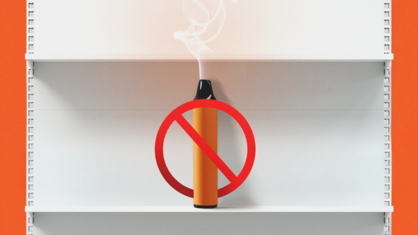 A vape with a ban symbol across it sits on a white shelf against an orange background | Botond Visnyei/Dreamstime/Fox Dsign/user13015019/Magnific/Mariam Zakaidze