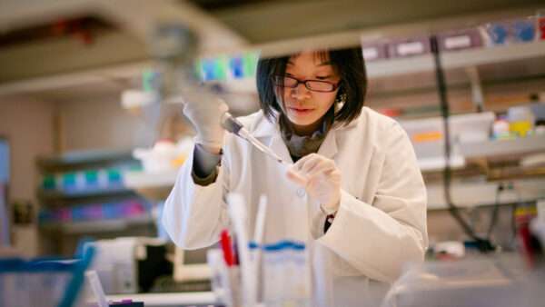 A photo of a woman in a white labcoat injecting something into a small clear tube. | Photo: Tommy Song/Dreamstime