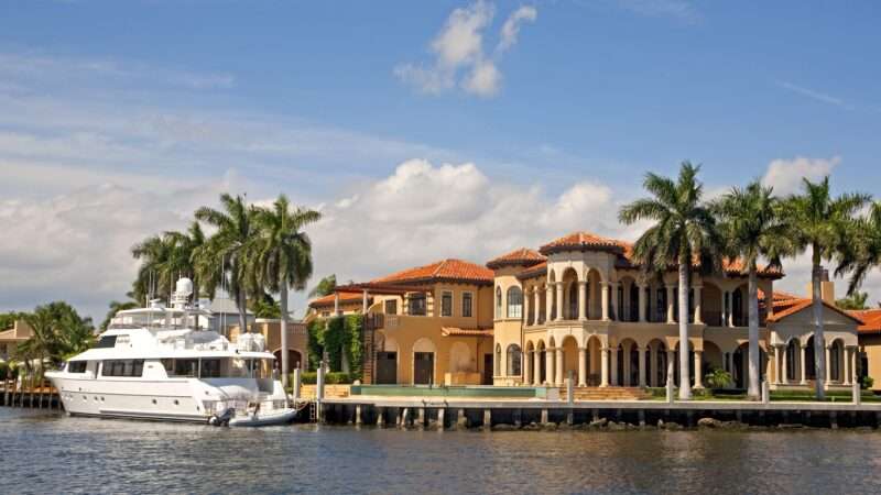 A luxury villa on the waterfront in Fort Lauderdale, with a boat and palm trees around it.