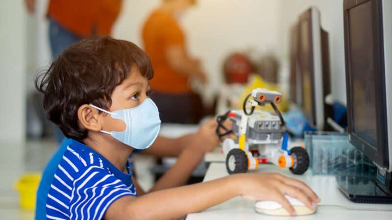 A masked student sits in front of a computer for virtual learning