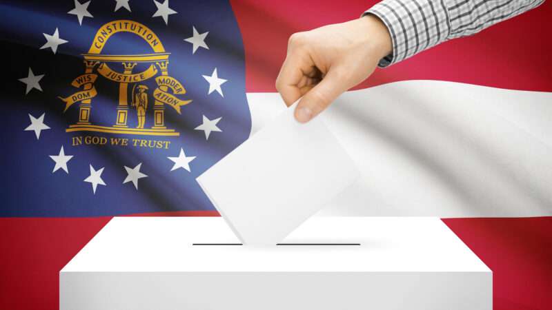 A hand casting a ballot in front of the Georgia state flag.