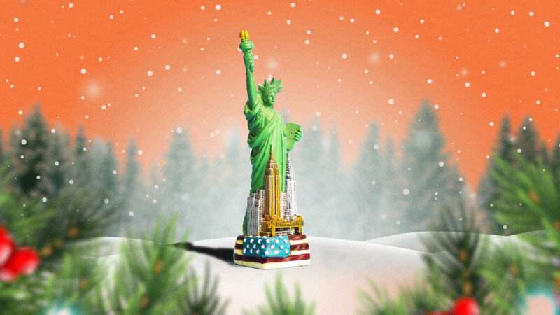 The Statue of Liberty surrounded by the New York City skyline sits in a snowy field with evergreen trees
