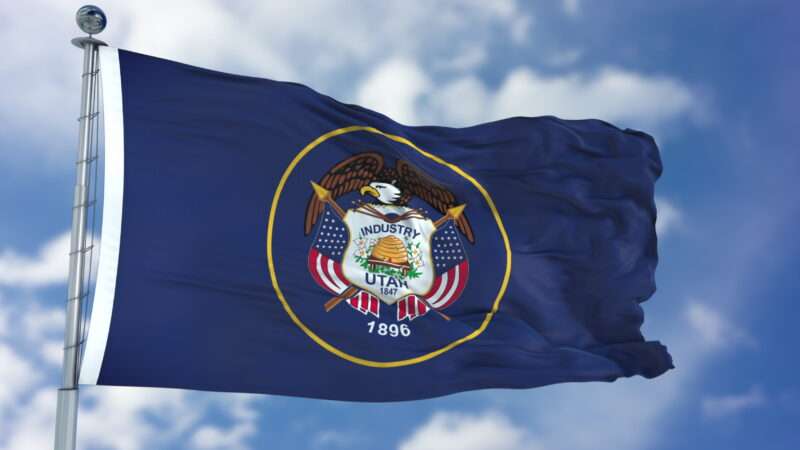 The State of Utah's flag against a partly cloudy sky.