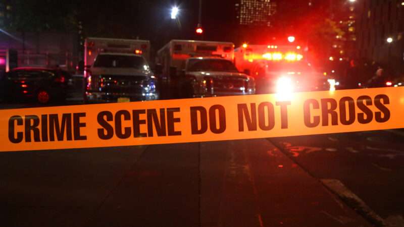 A nighttime picture with crime scene tape in the foreground and ambulances in the background.