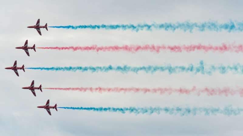 Five British Royal Air Forces jets fly in formation dispensing smokes of various colors. | Photokvu | Dreamstime.com