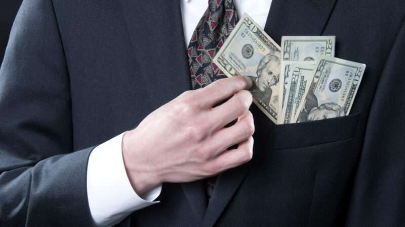 A man in a business suit pockets money. | Jeff Wasserman | Dreamstime.com