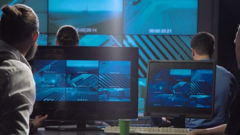 Several men sit in front of multiple monitors showing surveillance footage. | Framestock Footages | Dreamstime.com