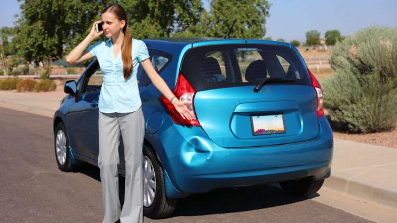 A woman stands by her dented car on the phone. | Printezis | Dreamstime.com