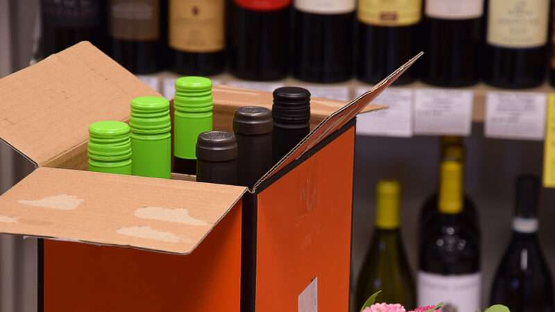 Box of wine bottles in front of a shelf with wine | Photo 209204568 © Martins Pormanis | Dreamstime.com