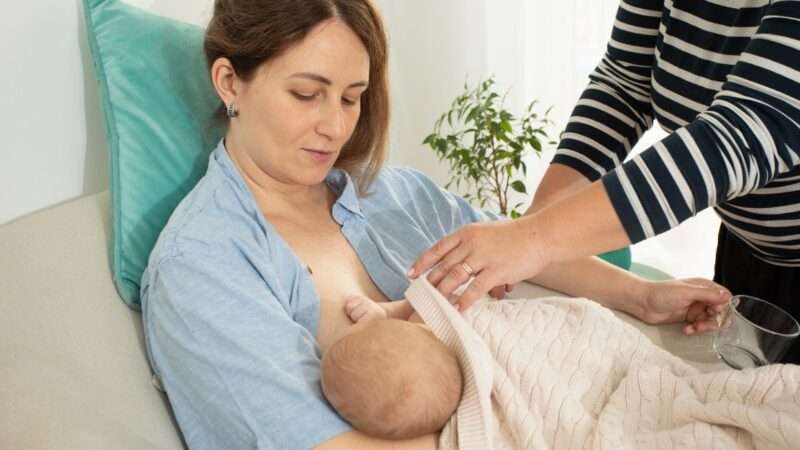 A woman breastfeeding while a consultant assists.