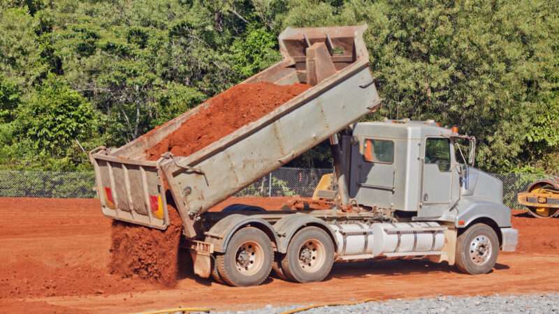 A tip truck dumping red soil at a construction site. | Johan Larson | Dreamstime.com