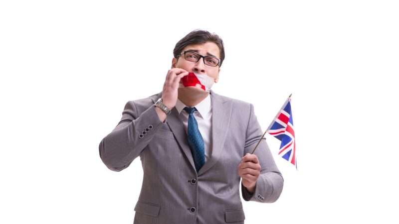 A businessman with tape over his mouth holding a flag of the United Kingdom.