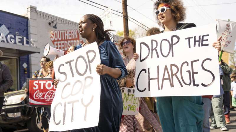 Anti-"Cop City" protesters hold signs that say STOP COP CITY and DROP THE CHARGES