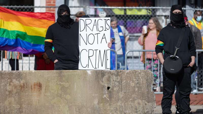 A man at a protest holding a sign that reads drag is not a crime" with a Pride flag in the background. | Michaal Nigro/ZUMAPRESS/Newscom