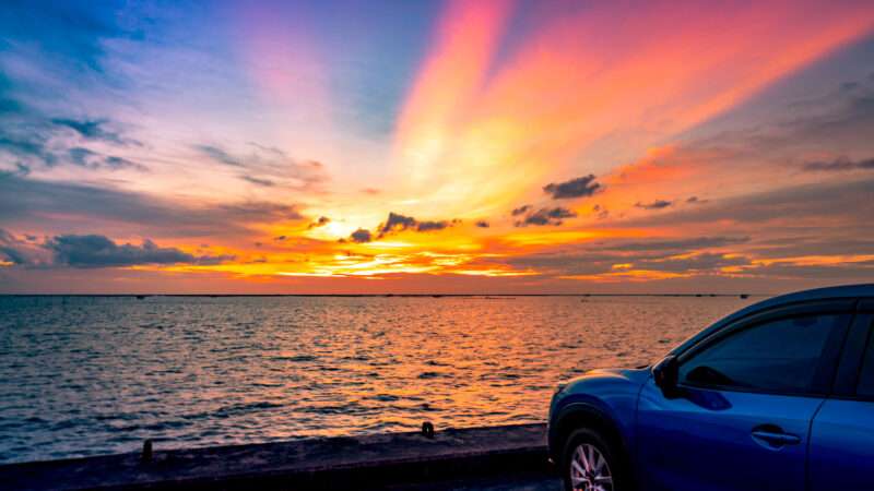 A compact blue car parked at the beach overlooking a picturesque sunset. | Artinun Prekmoung | Dreamstime.com
