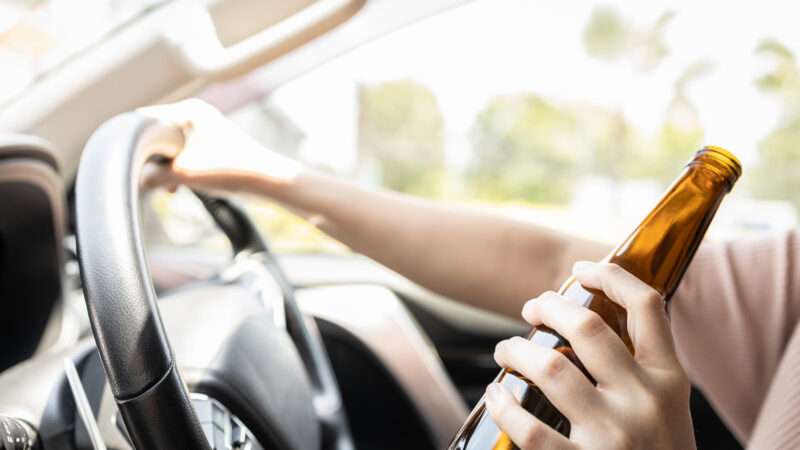 Close-up of a woman's hand holding a beer bottle while driving a car. | Satjawat Boontanataweepol | Dreamstime.com