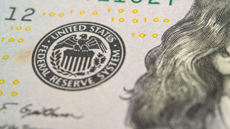A $100 bill is seen with the sign for the Federal Reserve System | sasirin/Newscom