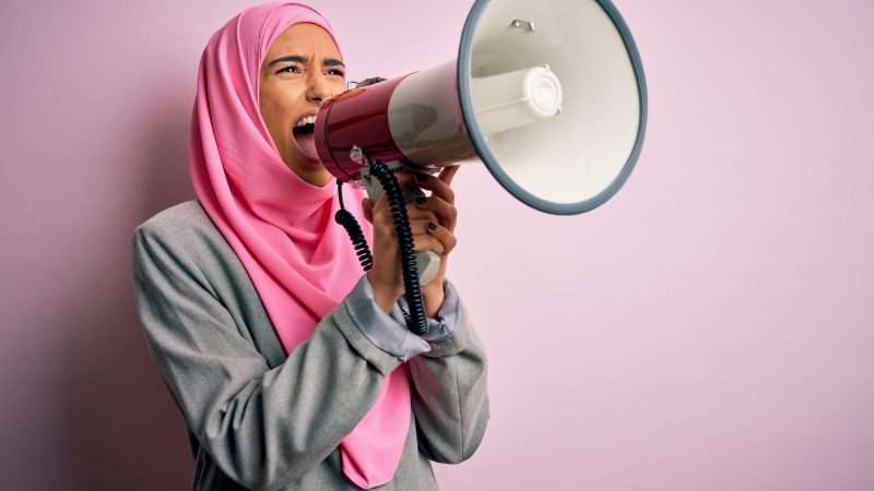 A woman in a pink hijab yell into a megaphone. | Aaron Amat | Dreamstime.com