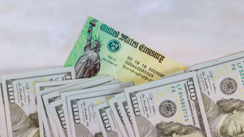 Several U.S. hundred-dollar bills on top of a U.S. Treasury check. | Photovs | Dreamstime.com