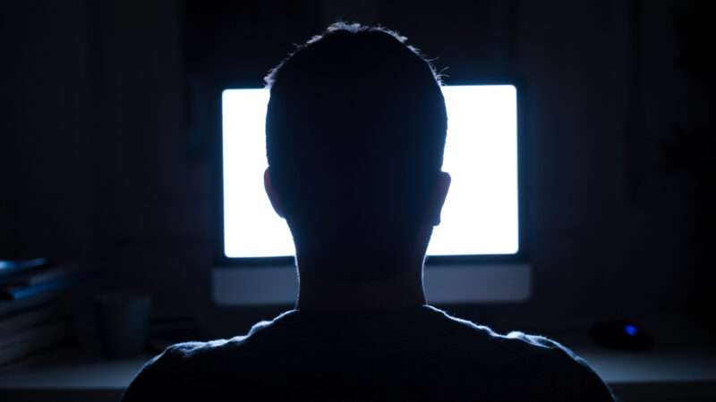 An unseen man sits in front of a computer screen at night. | F01photo | Dreamstime.com