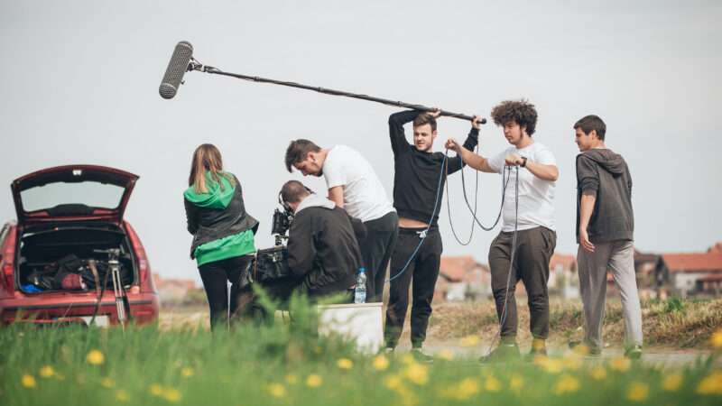 A group of young people shoot a film in an open field. | Guruxox | Dreamstime.com
