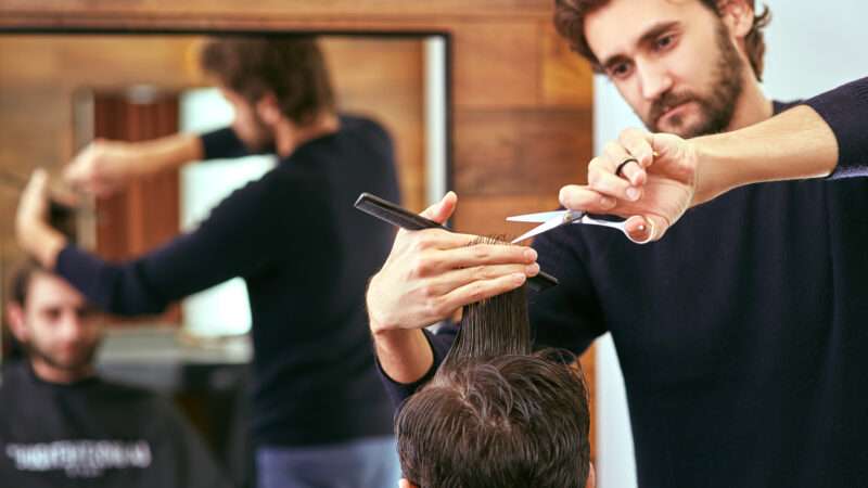 A barber cuts a man's hair with scissors. | Serhii Basyn | Dreamstime.com