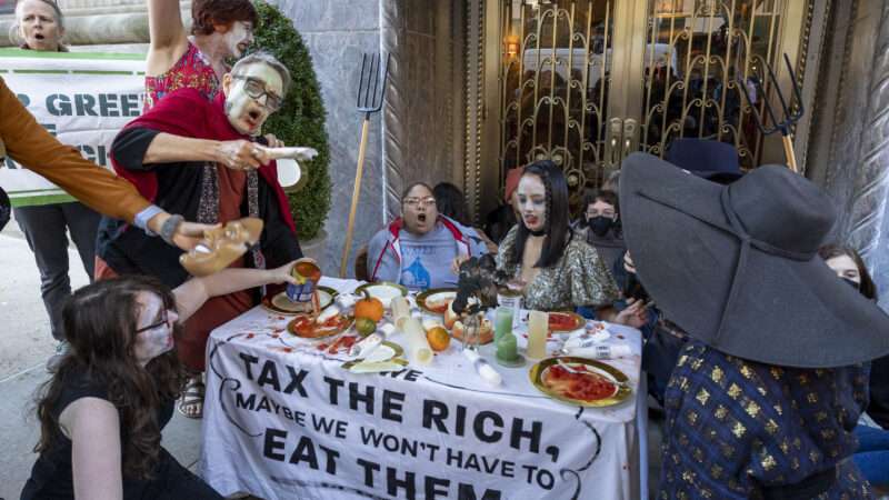 A group of protestors standing around a table that has a tablecloth reading "Tax the Rich" |  Gina M Randazzo/ZUMAPRESS/Newscom