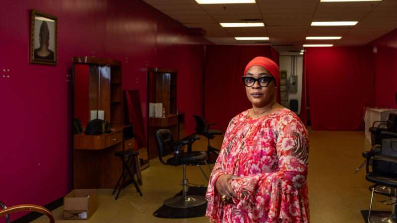 A woman stands in front of an empty hair salon, with her arms crossed and one hand over the other. | Photo: Institute for Justice