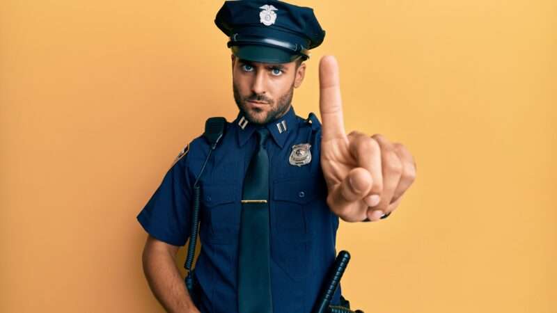 Male police officer holds up on finger to the camera, as if to say "hold on." | Aaron Amat | Dreamstime.com