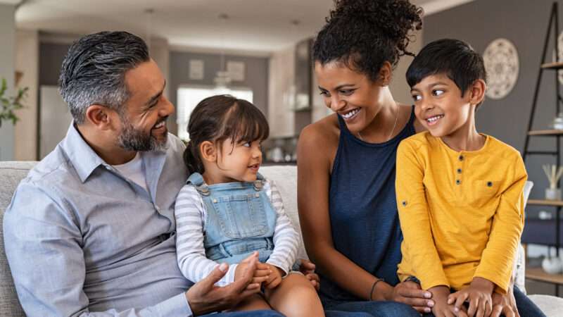 A young happy family of color, with father, mother, son, and daughter, sitting on a couch. | Rido | Dreamstime.com