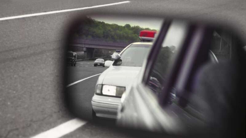 A police cruiser as viewed in a car's driver side view mirror. | Kentannenbaum | Dreamstime.com