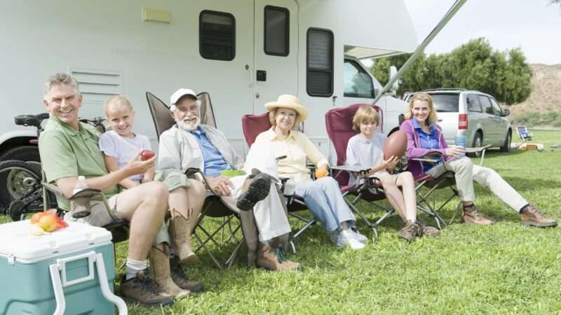 Several people sit in folding chairs outside a recreational vehicle | Photographerlondon | Dreamstime.com