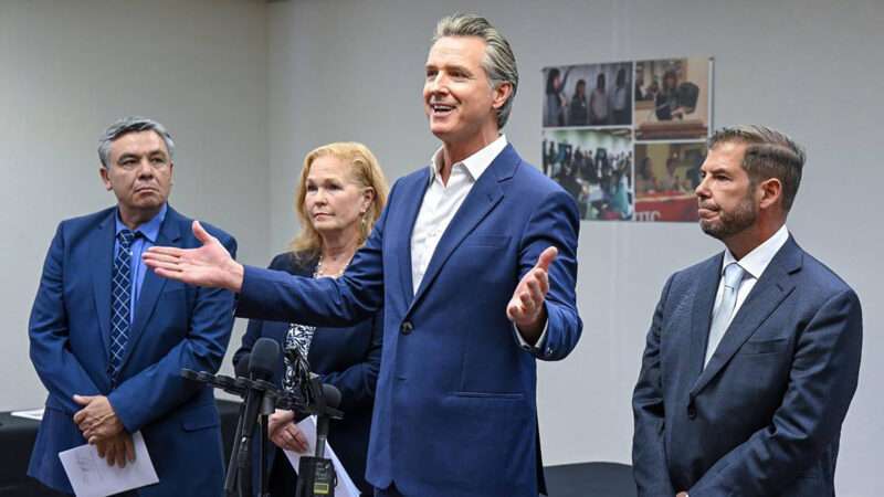 Gavin Newsom stands in front of several people and behind microphones | Craig Kohlruss/TNS/Newscom