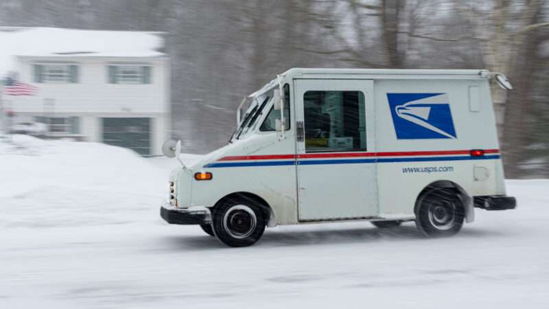 A United States Postal Service (USPS) mail truck driving in snow. The image is slightly blurred, suggesting a higher rate of speed. | Lequint | Dreamstime.com