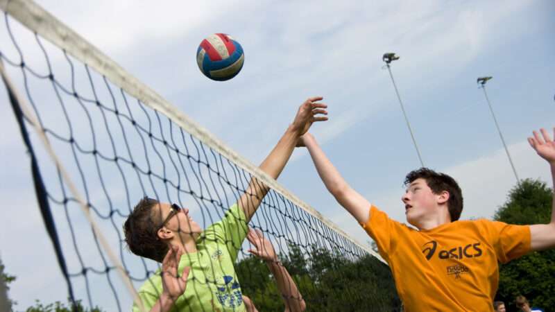 Two young men play volleyball up close to the net, each trying to hit the ball. | Sebastian Czapnik | Dreamstime.com